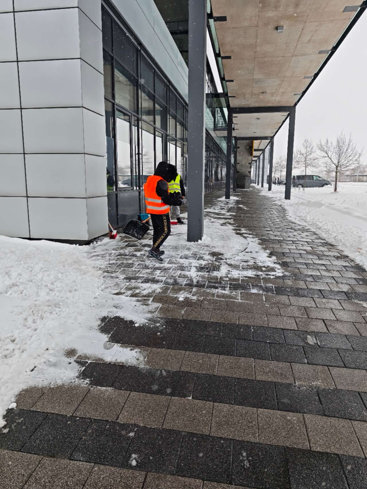 Workers clearing snow from a covered walkway at an industrial building